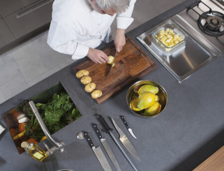 High angle view of male chef chopping kiwi on board at commercial kitchen counter